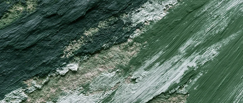 Close-up of rough concrete wall surface with peeling green paint and weathered texture