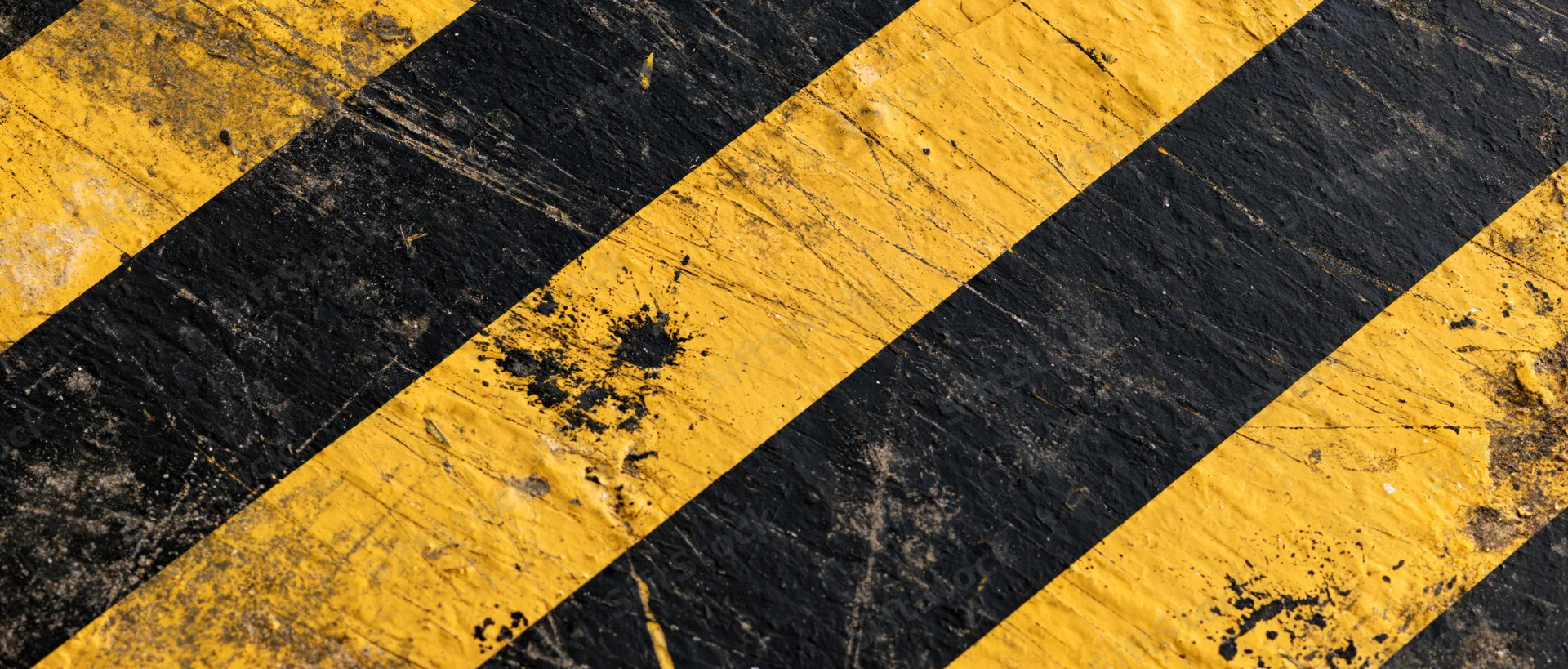 Diagonal yellow and black hazard stripes on a worn industrial pavement surface