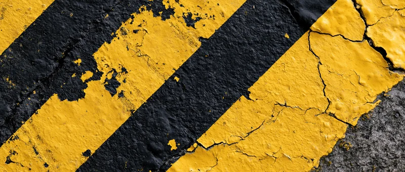 Close-up of weathered yellow and black striped hazard tape on cracked asphalt surface