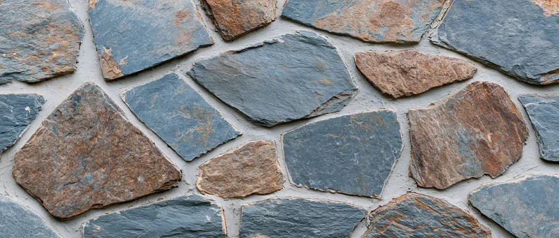 Close-up of irregular dry-stack stone wall with gray and brown stones set in mortarless pattern