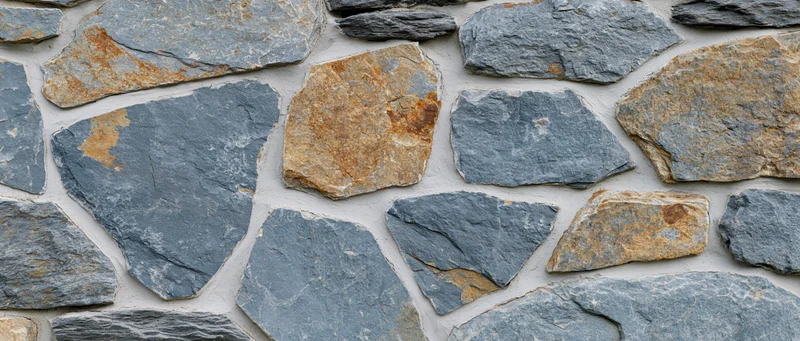 Close-up of irregular dry-stack stone wall with gray and brown rocks set in white mortarless pattern