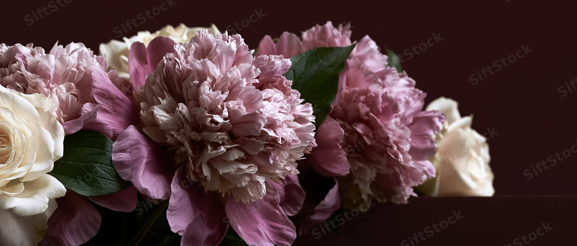 Close-up of dusty pink peony blooms and white roses clustered in a floral arrangement against a dark background