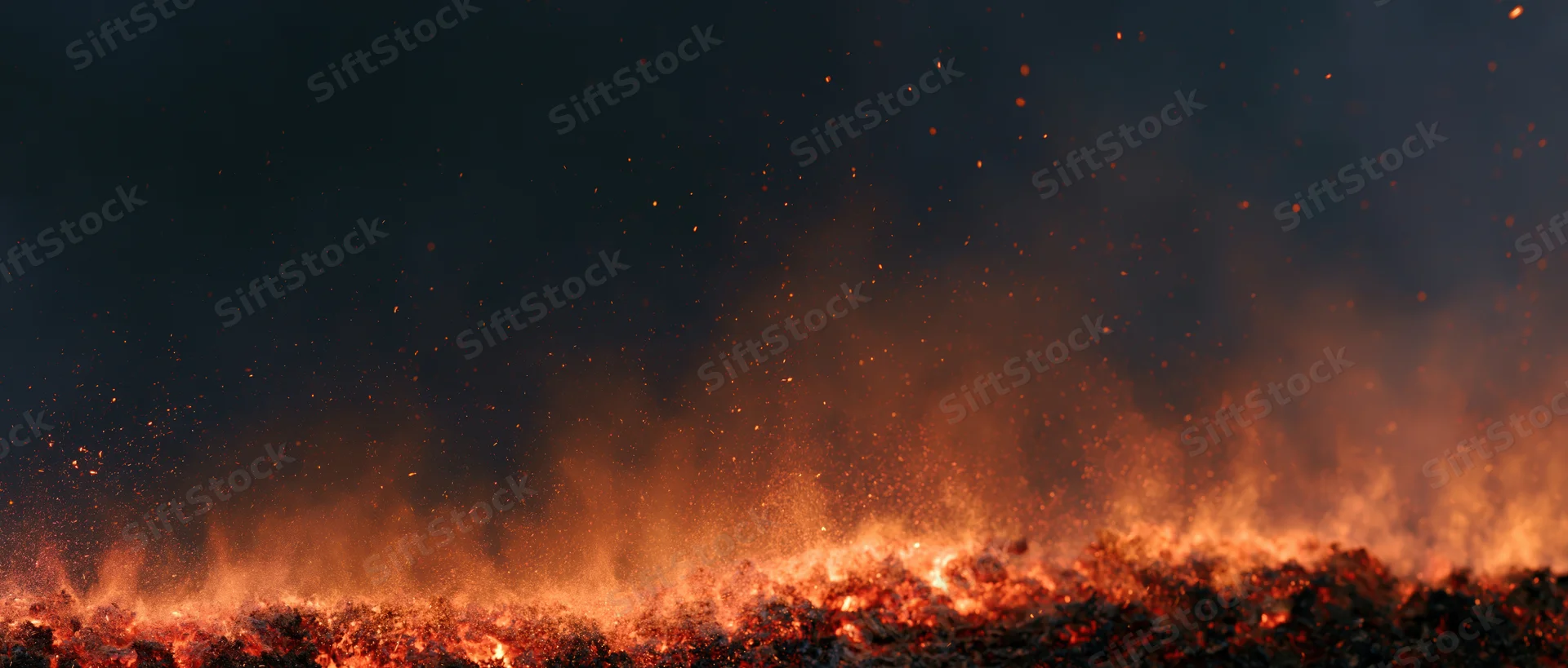 Fire flames erupting upward at night with sparks and smoke over dark landscape