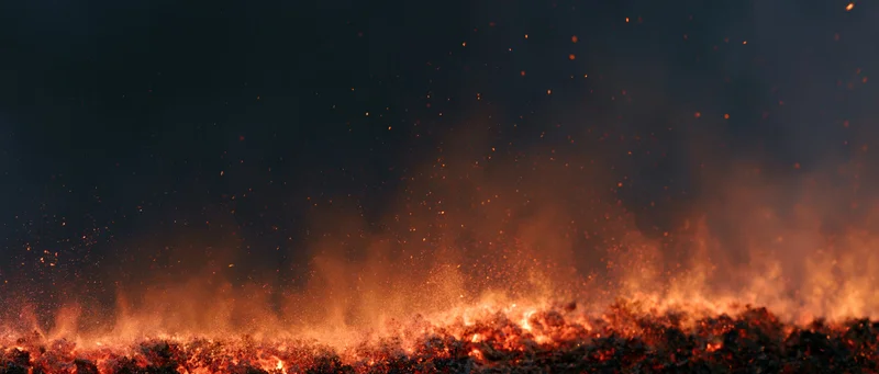 Fire flames erupting upward at night with sparks and smoke over dark landscape
