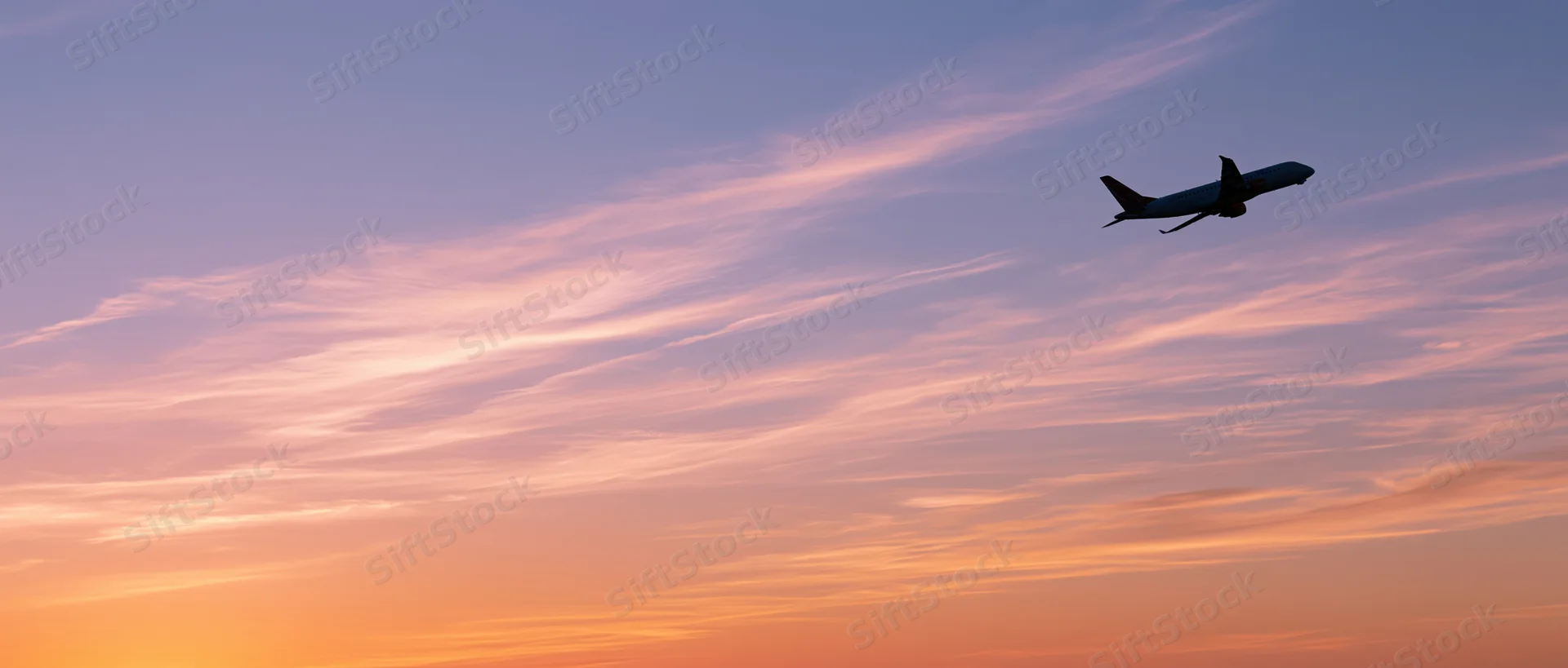 Commercial passenger jet climbing in silhouette against a colorful sunset sky