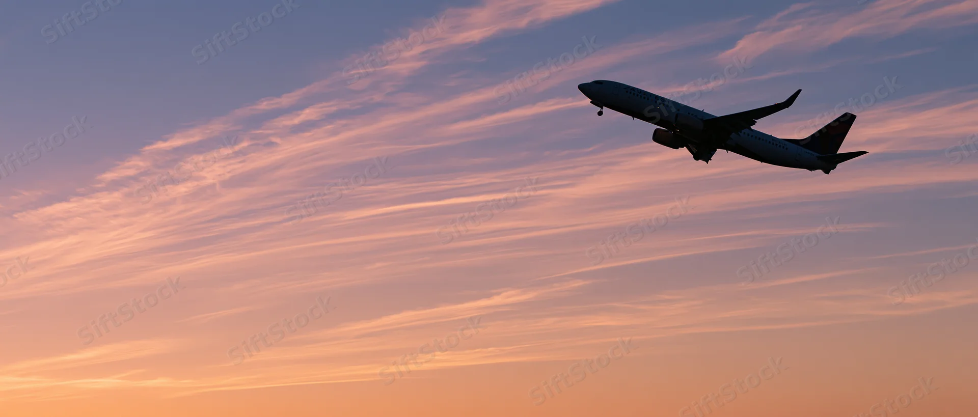 Commercial passenger jet climbing in silhouette against a colorful sunset sky
