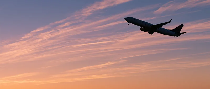 Commercial passenger jet climbing in silhouette against a colorful sunset sky