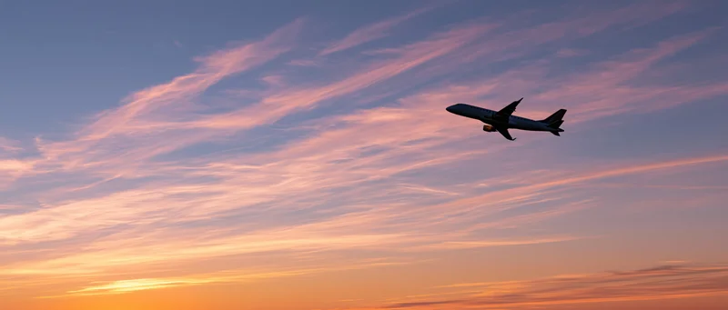 Commercial passenger jet climbing in silhouette against a colorful sunset sky