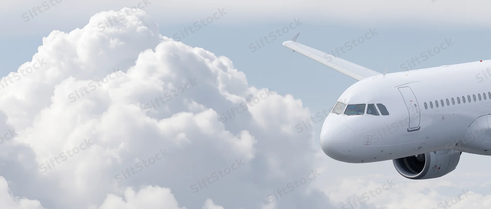 Commercial passenger jet cruising at altitude with nose and wing visible against clouds and sky