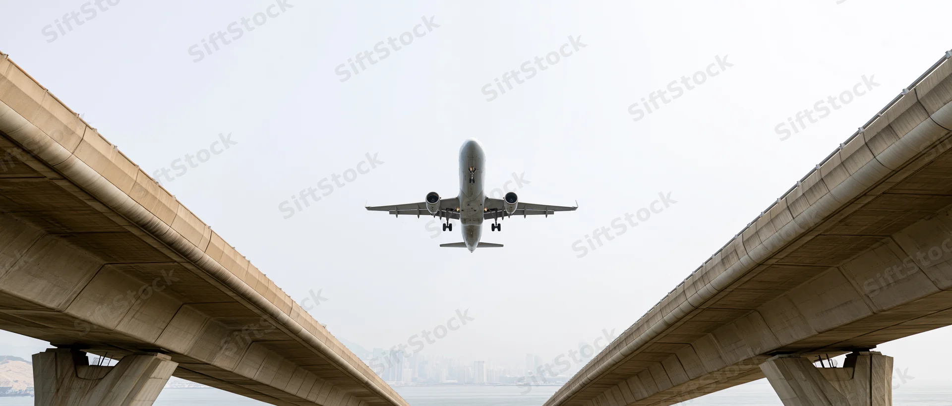 Commercial passenger jet descending between two concrete overpasses toward airport runway