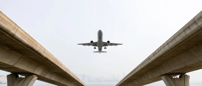 Commercial passenger jet descending between two concrete overpasses toward airport runway