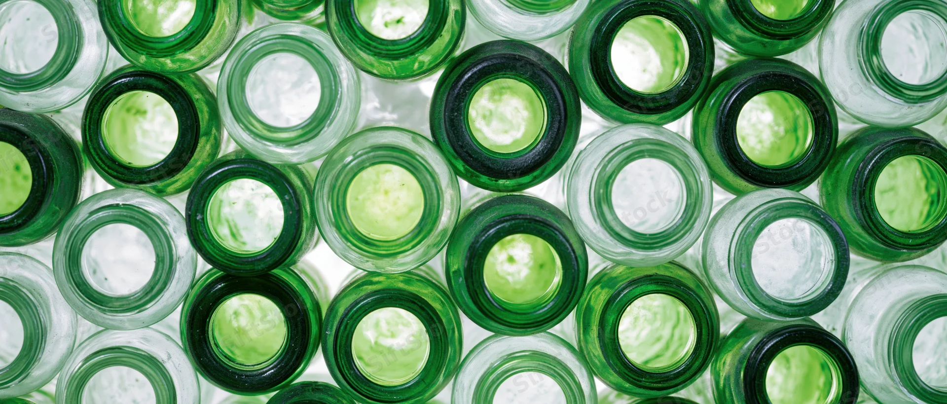 Overhead view of empty green glass bottles arranged in a repeating pattern on a white surface