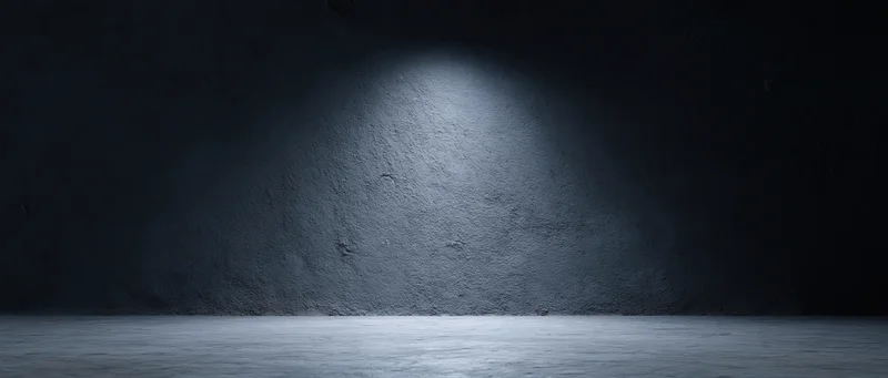 Spotlight on rough concrete wall in dark empty studio room