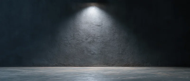 Spotlight on rough concrete wall in dark empty studio room