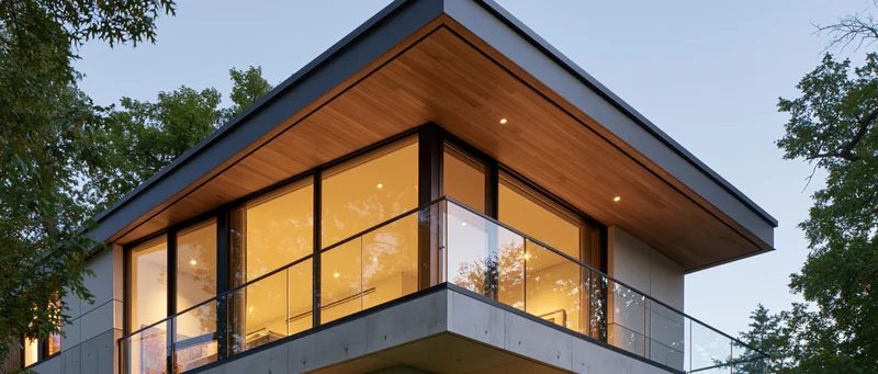 Modern house exterior corner with glass windows and balcony surrounded by trees at evening