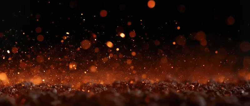 Glowing embers and sparks rising from dark ground against black background