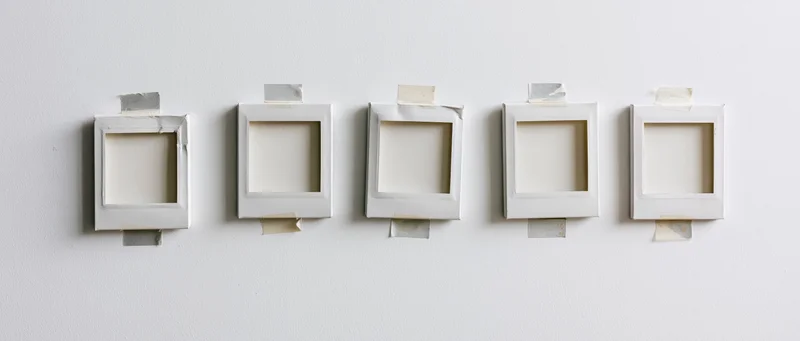 Five blank instant film photo frames taped in a row on a white wall