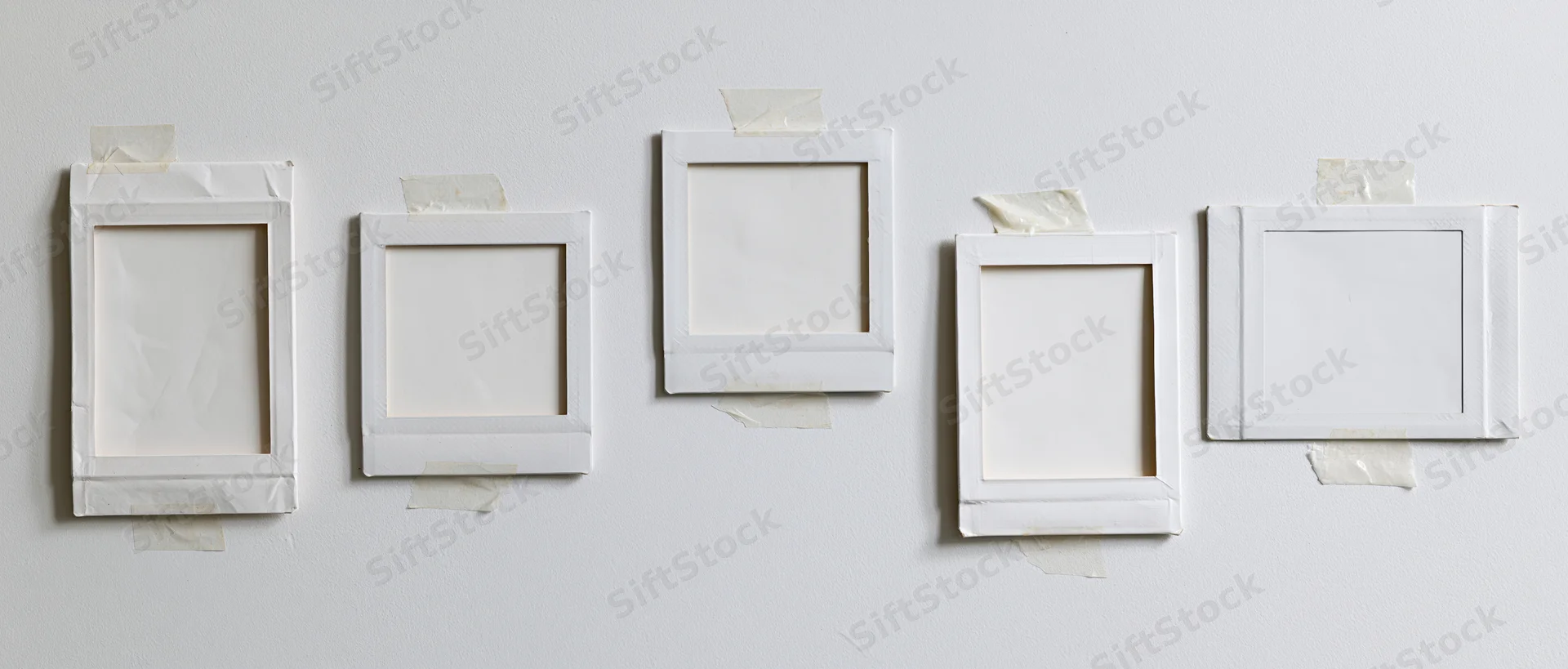 Five blank white instant photo frames taped in a row on a plain white wall