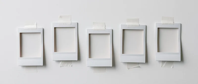 Five blank instant photo frames taped to a white wall in a horizontal row