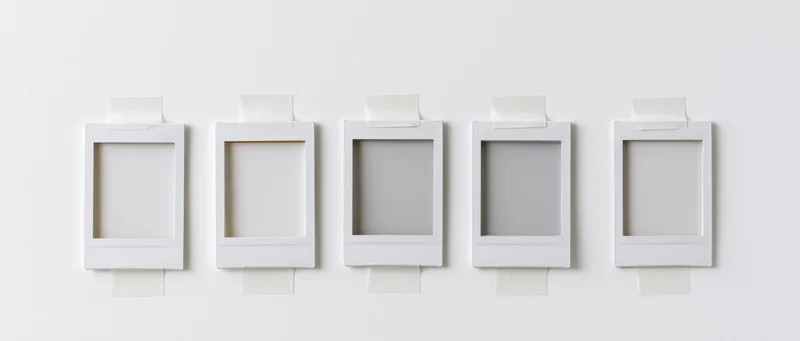 Five blank instant photo frames with white borders taped to a white wall in a row