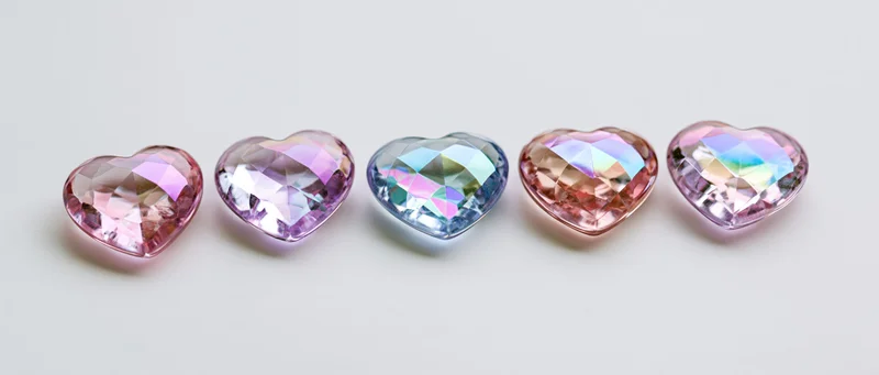 Five heart-shaped crystal gemstones arranged in a row on a white surface