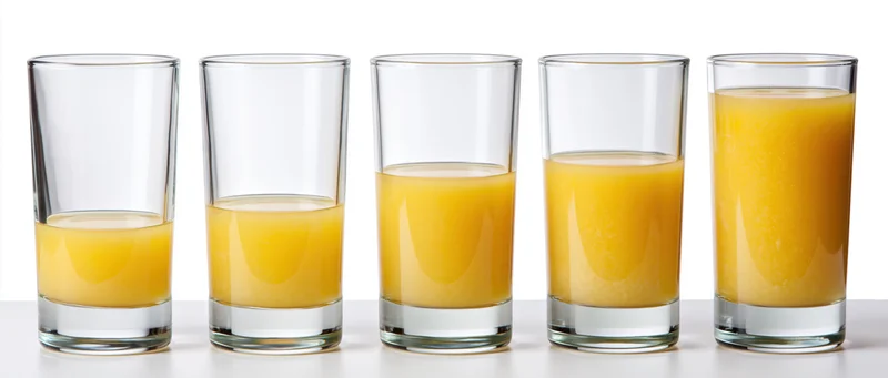 Five identical glasses filled with increasing amounts of orange juice in a row on a white surface