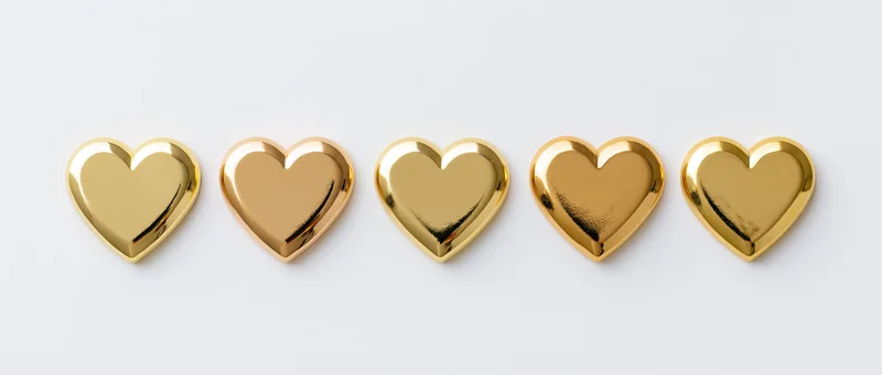 Five polished gold metal hearts arranged in a horizontal row on a white surface