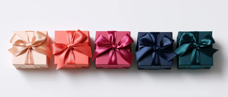 Five square gift boxes in a row wrapped in colored paper with satin bows on white background