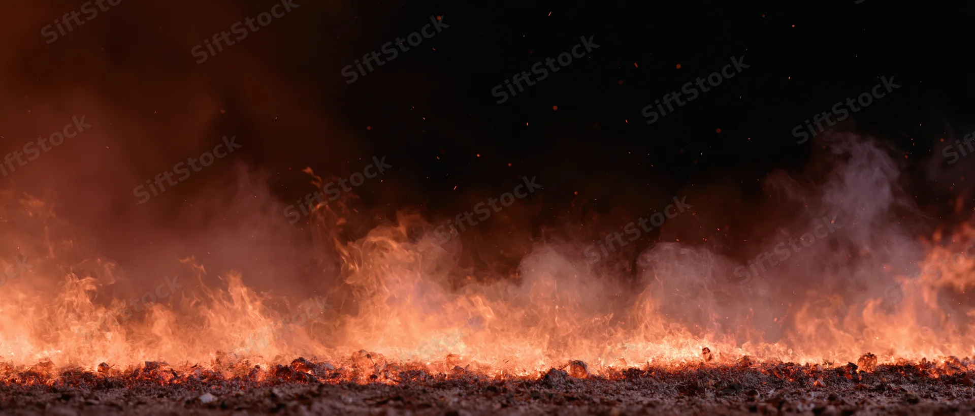 Flames and embers rising from burning ground at night