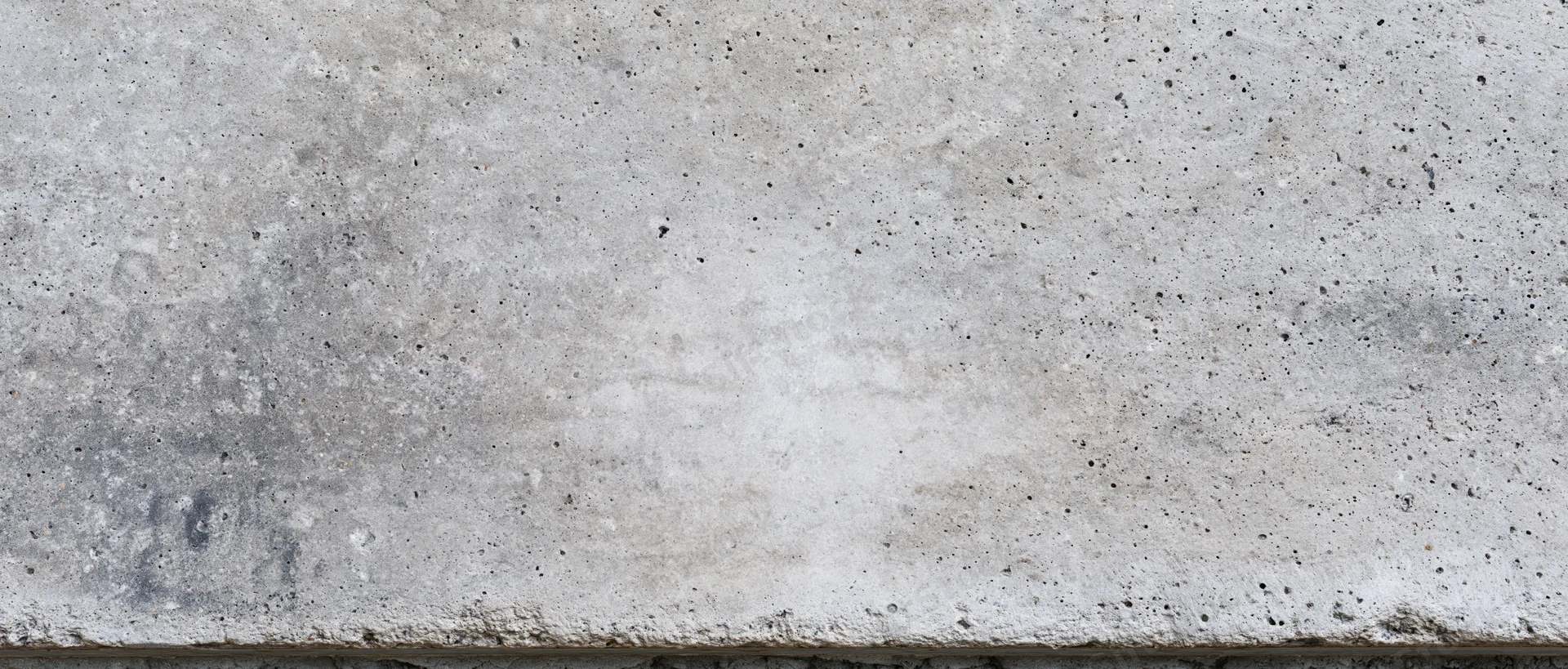 Wide panoramic view of a flat concrete wall surface with rough texture and speckled gray finish