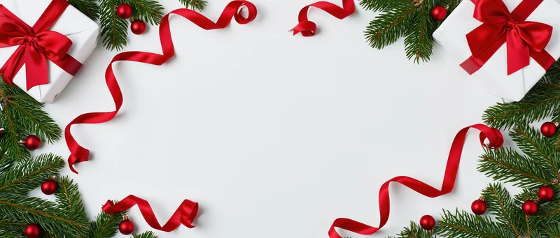 Christmas border arrangement with pine branches, red ribbons, and wrapped gifts on white surface
