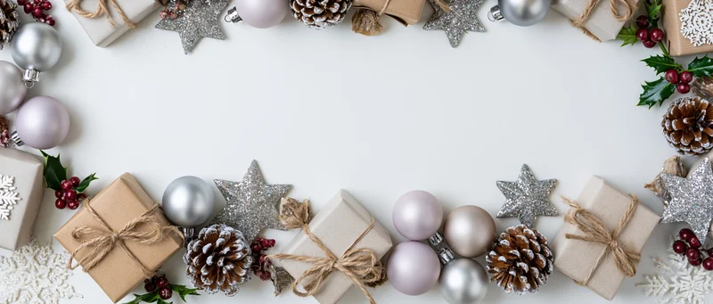 Christmas border arrangement with ornaments, gifts, pinecones and holly on white surface