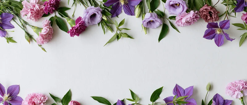 Loose purple and pink flowers arranged along the top and bottom edges of a white surface, forming a floral border with copyspace in the center