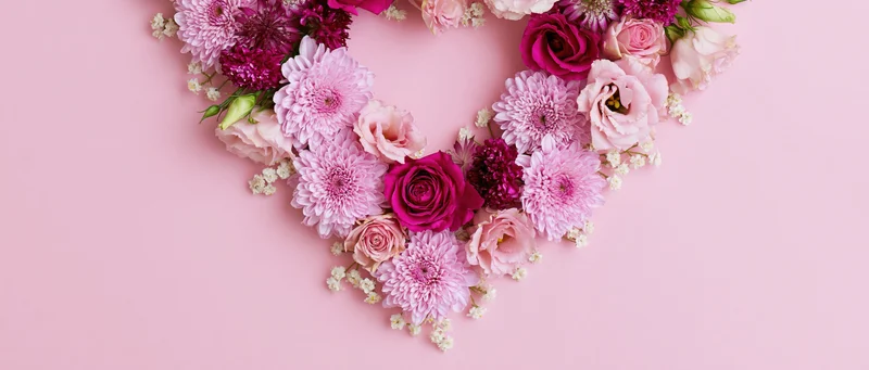 Heart-shaped floral arrangement of pink roses and chrysanthemums on a soft pink background with copyspace