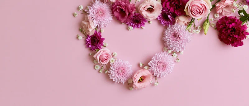 Mixed flowers arranged in heart shape on pink background