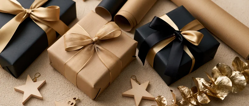 Three wrapped gift boxes with ribbons and decorative stars arranged on a beige surface in a flat lay composition