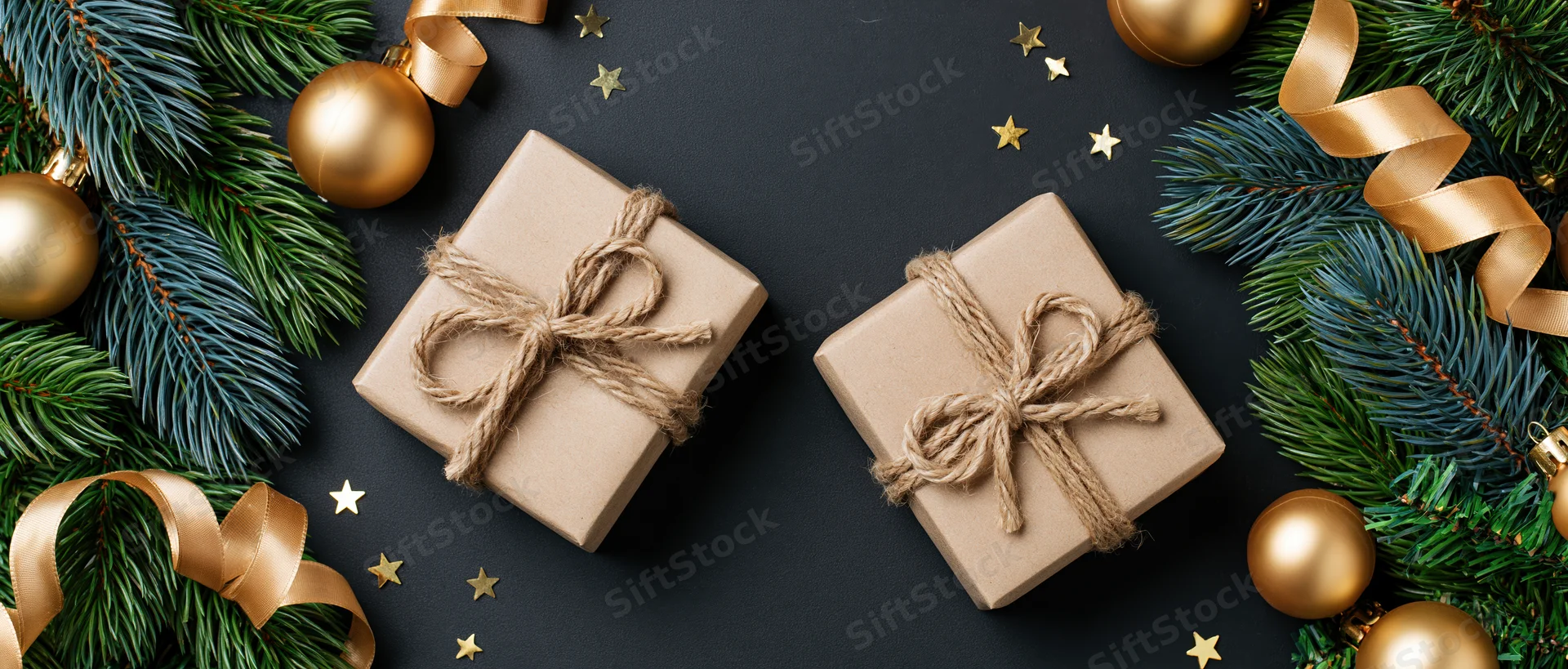 Two kraft paper gift boxes tied with twine bows on dark surface surrounded by pine branches, gold ornaments and stars
