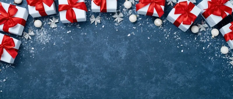 White gift boxes with red ribbons arranged along top of blue textured surface with snow and ornaments, copyspace below