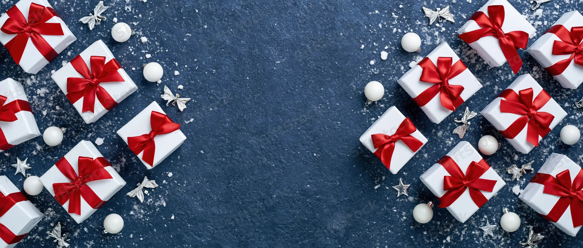 White gift boxes with red satin ribbon bows arranged on dark blue surface with silver stars and white ornaments, copyspace in center