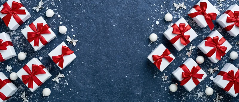 White gift boxes with red satin ribbon bows arranged on dark blue surface with silver stars and white ornaments, copyspace in center