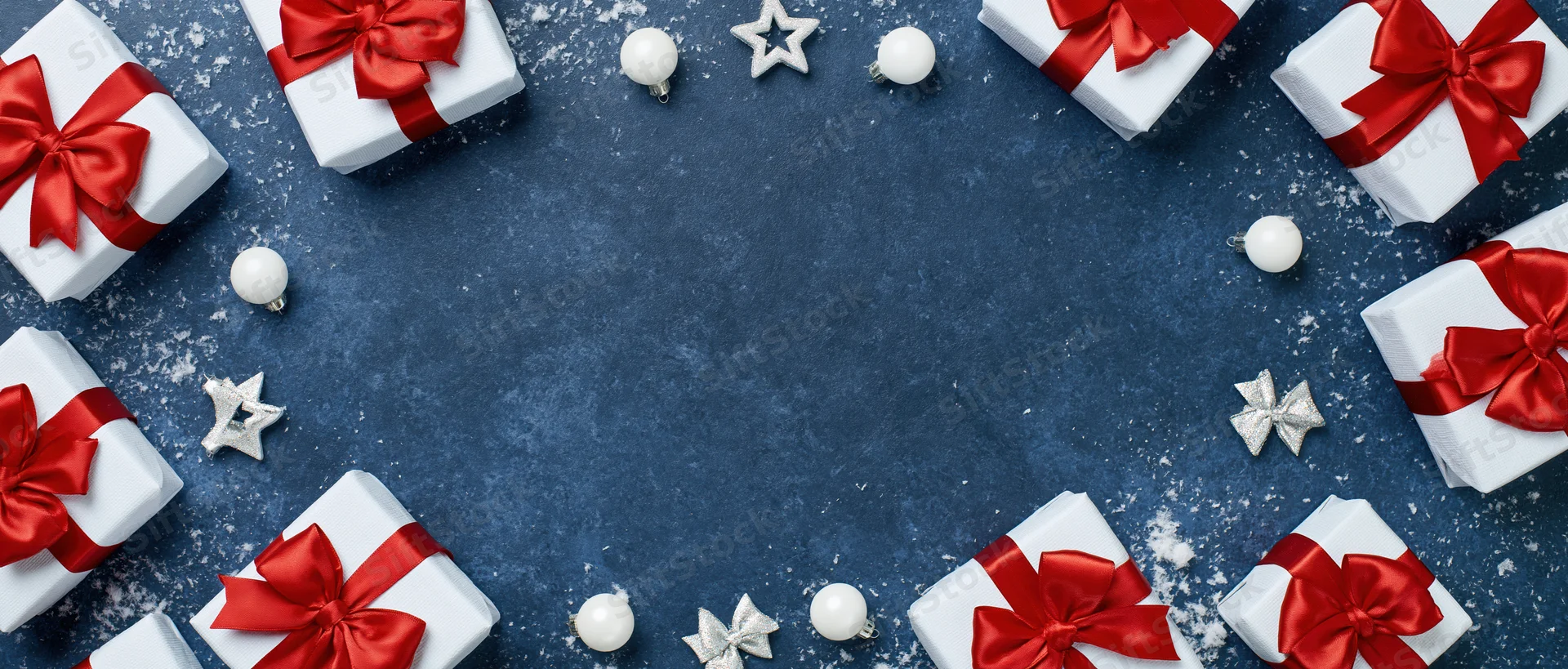 White gift boxes with red ribbons arranged in a circle on blue surface with ornaments and snow, flat lay view