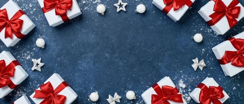 White gift boxes with red ribbons arranged in a circle on blue surface with ornaments and snow, flat lay view