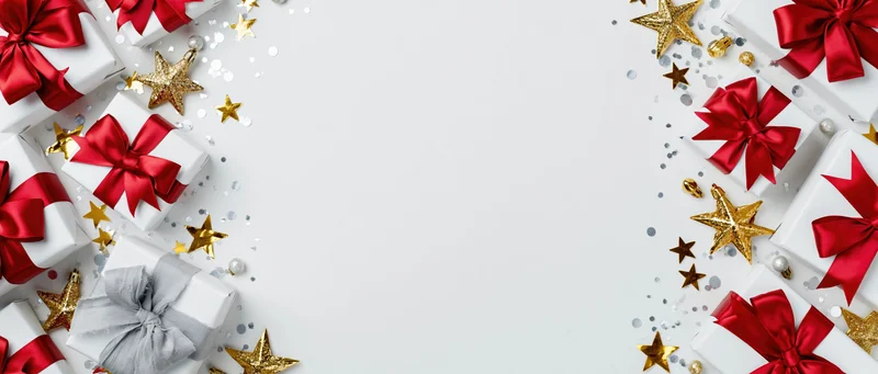 White gift boxes with red satin bows and gold stars arranged along edges on white background with central copyspace