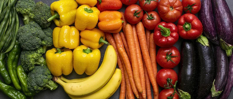 Overhead flat lay of fresh fruits and vegetables arranged on dark surface