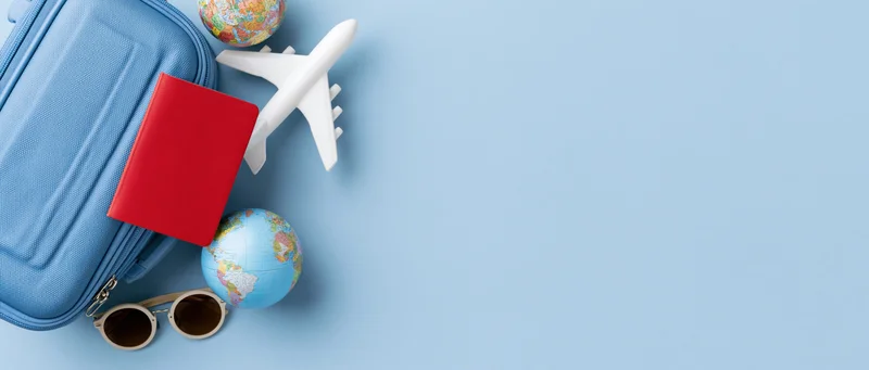 Travel items including suitcase, passport, airplane, globe and sunglasses arranged on blue surface with copyspace