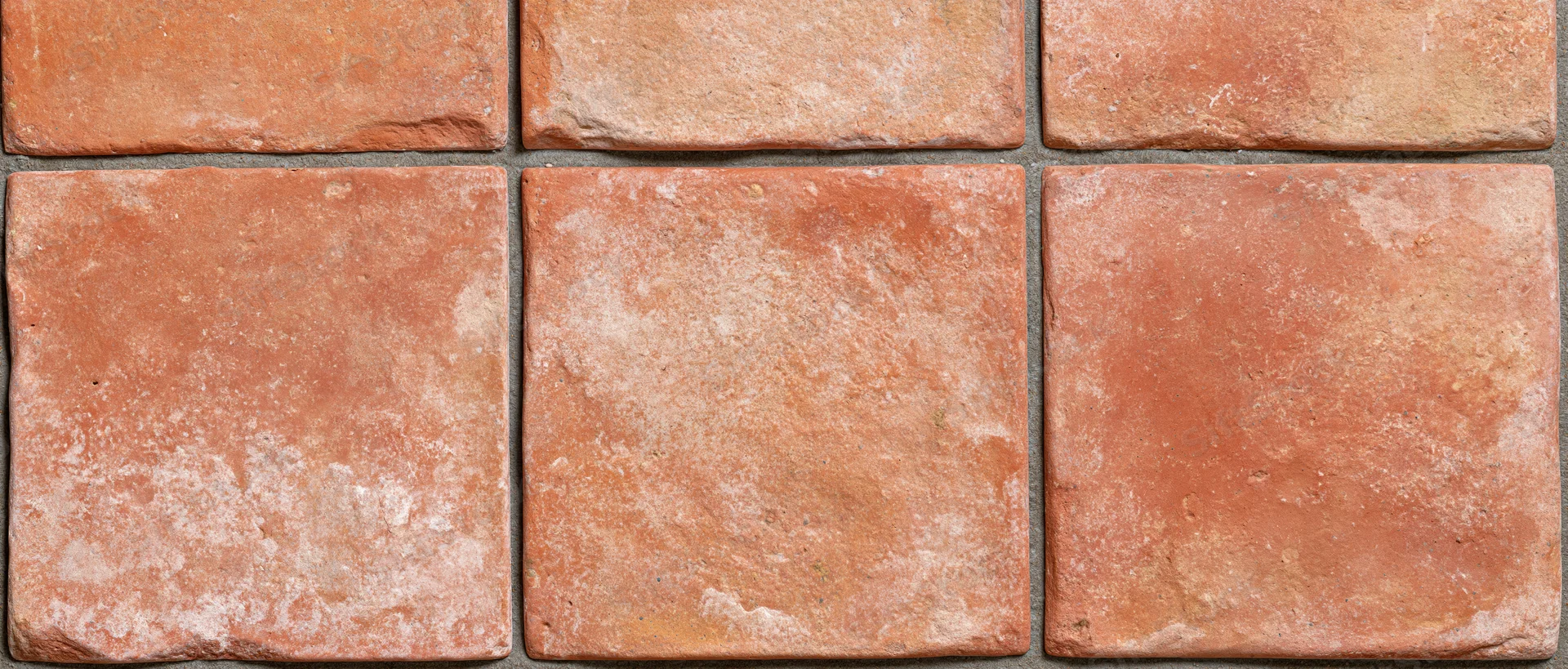Aged terracotta tiles arranged in a grid pattern on a floor surface