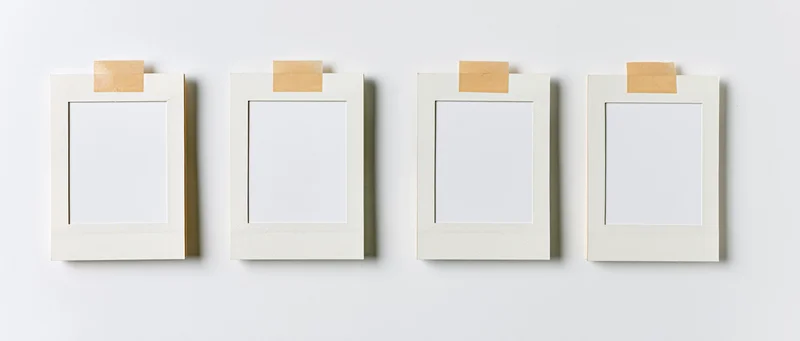 Four blank white instant photo frames arranged in a row on a white wall