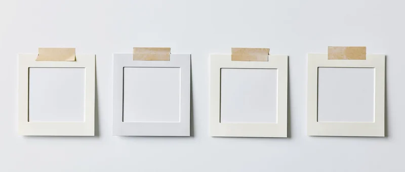 Four blank white instant photo frames arranged in a row on a plain wall