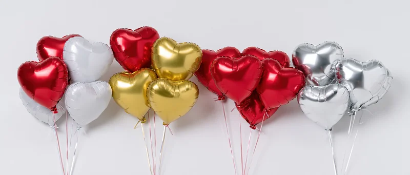 Heart-shaped foil balloons in red, gold, silver and white arranged in bunches against a white background