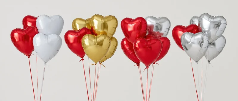 Four bunches of heart-shaped foil balloons in red, silver, gold and white arranged in a row against a plain background